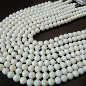 May include: A strand of white round beads, made of natural shell, with a smooth, polished finish. The beads are strung on a clear thread and are arranged in a circular pattern.
