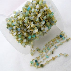 May include: A spool of gold chain with aqua blue and green gemstone beads. The chain is strung with small, irregular shaped beads.