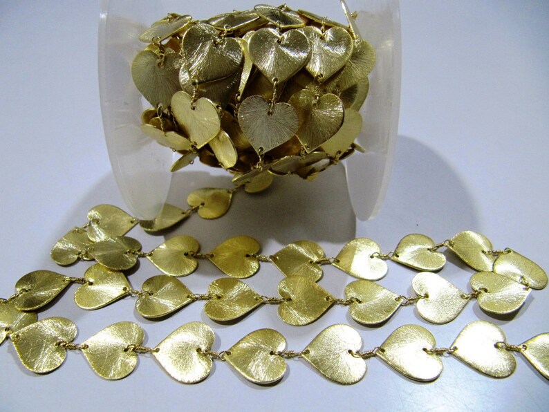 May include: A spool of gold-colored heart-shaped metal chain trim. The chain is made of small, interconnected hearts, and the hearts have a slightly textured surface.