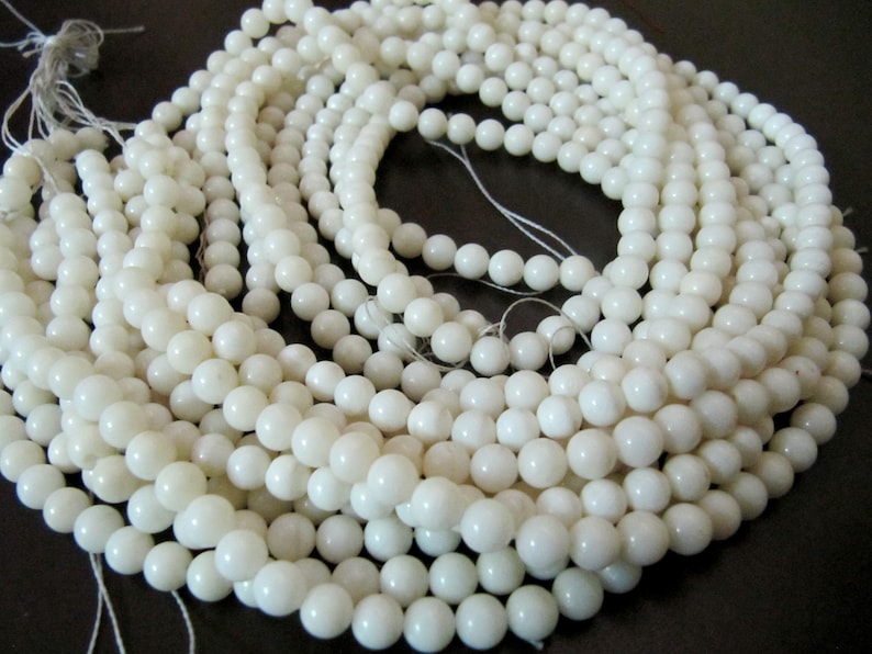 May include: A strand of white round beads made from natural shell. The beads are smooth and polished, and they are strung on a white thread.