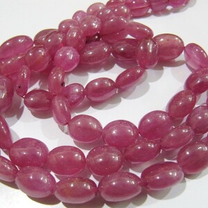 May include: A strand of pink oval-shaped gemstone beads. The beads are smooth and polished, with a slight sheen.