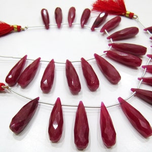 Puede incluir: Una hebra de 24 cuentas de piedra preciosa de color rojo rubí, facetadas y en forma de lágrima. Las cuentas están enhebradas en un alambre de plata y tienen un acabado pulido.