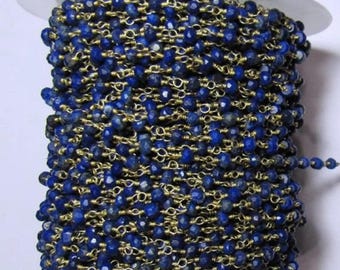 May include: A spool of faceted, deep blue lapis lazuli beads strung on gold-colored wire. The beads are tightly wound around a clear plastic spool, creating a dense, textured appearance. The gold wire adds a contrasting metallic sheen.