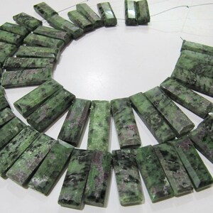 May include: A strand of green, black, and pink gemstone beads. The beads are rectangular and have a faceted finish. The beads are strung on a wire and are ready to be made into jewellery.