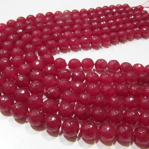 Puede incluir: Primer plano de varios hilos de cuentas facetadas de color rojo intenso. Las cuentas son redondas y tienen una superficie pulida. Están ensartadas en un hilo fino de color rosa. Las cuentas están muy juntas, creando una apariencia texturizada. Ideal para la creación de joyas.