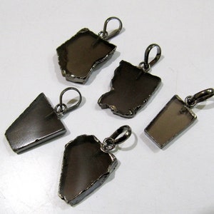 Könnte beinhalten: Fünf schwarze Metallanhänger mit unregelmäßigen Formen und silberfarbenen Metallscharnieren. Die Anhänger bestehen aus einem dunklen, undurchsichtigen Material, das wie Stein aussieht.