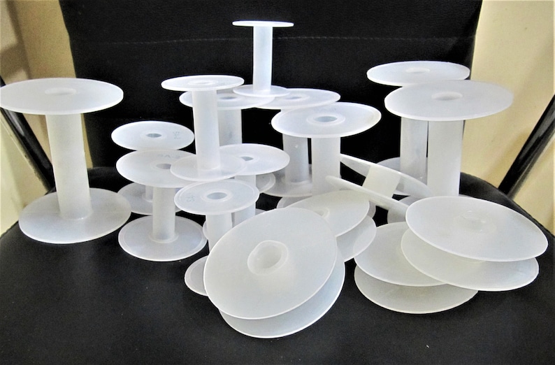 May include: A pile of white plastic spools for thread or yarn. The spools are various sizes and are stacked on top of each other.