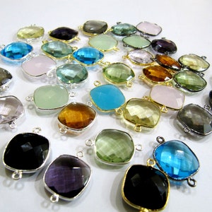 Puede incluir: Una colección de colgantes de piedras preciosas de corte cuadrado en varios colores, incluyendo azul, verde, rosa y ámbar. Cada colgante tiene un marco de metal plateado o dorado con bucles para sujetar a una cadena u otra pieza de joyería.