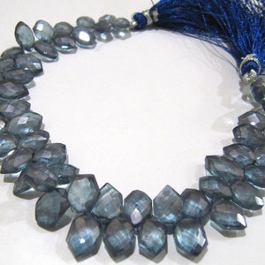 May include: A strand of faceted blue topaz beads with a blue tassel. The beads are a teardrop shape and have a shimmery finish.