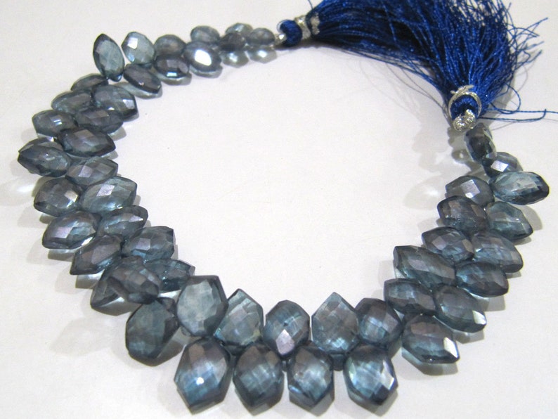 May include: A strand of faceted blue topaz beads with a blue tassel. The beads are a teardrop shape and have a shimmery finish.