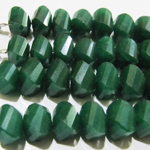 Puede incluir: Una hebra de cuentas de piedras preciosas facetadas de color verde oscuro. Las cuentas tienen un diámetro aproximado de 10 mm y un acabado liso y pulido.