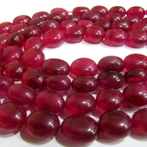 May include: A strand of deep red gemstone beads. The beads are oval shaped and have a smooth, polished finish.