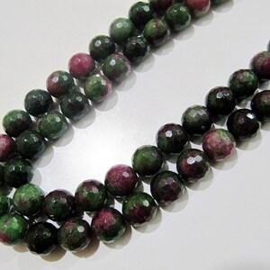 May include: A strand of green and pink gemstone beads. The beads are faceted and have a round shape. The beads are strung on a clear thread.