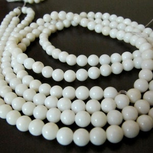 May include: A strand of white shell beads, strung on a white thread. The beads are round and smooth, and they are arranged in a circular pattern.