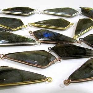 May include: A collection of 16 dark gray labradorite gemstone pendants with gold, silver, and black metal accents. Each pendant has a faceted, teardrop shape and two jump rings for attaching to jewelry.
