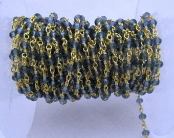 May include: A close-up of a gold chain with dark blue glass beads. The chain is coiled and ready to be used for jewelry making.