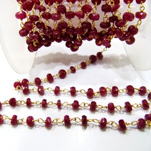 Könnte beinhalten: Eine Strähne aus rubinroten Edelsteinperlen, die auf einer goldenen Kette aufgefädelt sind. Die Perlen sind facettiert und haben eine leicht unregelmäßige Form. Die Kette ist zart und hat ein klassisches Gliederdesign.