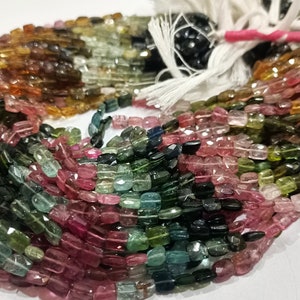 Puede incluir: Una hebra de cuentas de turmalina multicolores. Las cuentas son facetadas y tienen una forma rectangular. Los colores de las cuentas incluyen verde, rosa, marrón y negro.