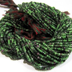 May include: A strand of green and purple gemstone beads. The beads are small and round, and they are strung on a thin thread. The beads are a mix of green and purple, and they have a slightly iridescent sheen.