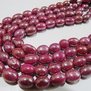 May include: A strand of deep red ruby beads, each bead is oval shaped and has a smooth, polished finish.