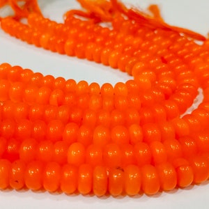 Könnte beinhalten: Eine Strähne aus leuchtend orangefarbenen runden Perlen aus Glas oder Kunststoff liegt auf einer weißen Oberfläche. Die Perlen sind glatt und glänzend, und die Strähne ist dick und voll.