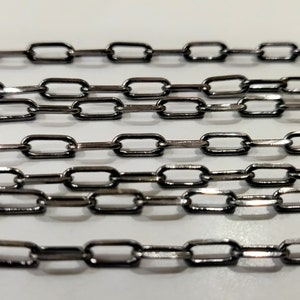 May include: A close-up of a silver chain with black links. The chain is made of small, rectangular links that are connected together to form a continuous chain.
