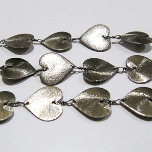 May include: A silver necklace with a chain made of small, connected heart-shaped charms.