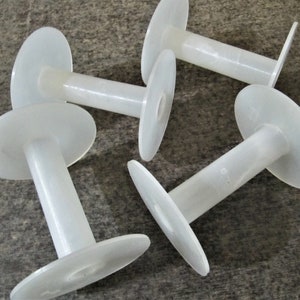 May include: Four white plastic spools for thread or yarn. The spools are all the same size and shape, with a large, flat circular base and a smaller, cylindrical center.