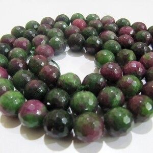 May include: A strand of faceted green and pink gemstone beads. The beads are round and have a smooth, polished finish.