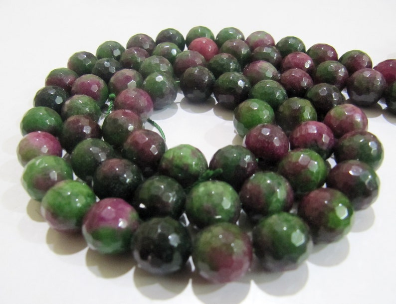 May include: A strand of faceted green and pink gemstone beads. The beads are round and have a smooth, polished finish.