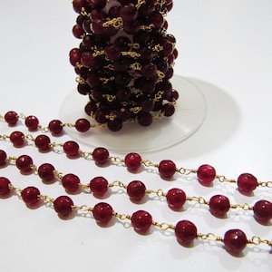 May include: A strand of red gemstone beads with gold chain links. The beads are round and have a slightly faceted appearance. The chain is delicate and has a subtle shine.