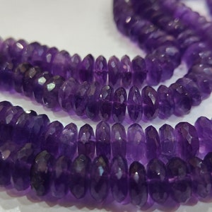 May include: A strand of purple amethyst beads, each bead is faceted and has a slightly pointed shape. The beads are strung together to form a long necklace.