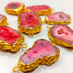 May include: Seven pink and white agate slices with gold-plated edges and jump rings. The agate slices are irregular in shape and have a natural, organic look.