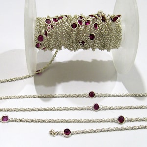 Puede incluir: Un carrete de cadena de plata con pequeñas piedras preciosas redondas de color rosa unidas. La cadena está dispuesta en línea recta, mostrando el espaciado de las piedras preciosas.