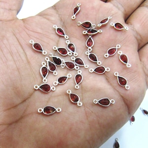 Peut inclure: Une collection de breloques en forme de goutte de pierre rouge avec des anneaux de saut en argent. Les breloques sont éparpillées sur une main.