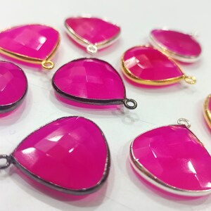 May include: A group of pink gemstone pendants with gold and silver accents. The pendants are teardrop shaped and have a faceted design.