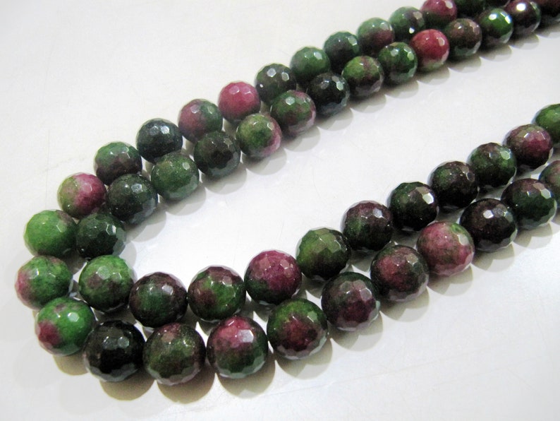 May include: A strand of green and pink gemstone beads. The beads are faceted and have a round shape.