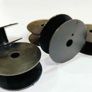 May include: Five black plastic spools for thread or yarn. The spools are stacked on top of each other.