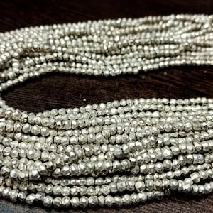 Puede incluir: Una hebra de cuentas de pirita plateada, cada cuenta está facetada y tiene una forma rugosa e irregular. Las cuentas están enhebradas en un cordón blanco y están listas para ser utilizadas para la elaboración de joyas.