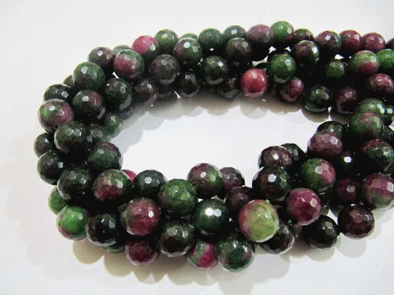 May include: A strand of faceted green and pink gemstone beads. The beads are round and have a polished finish.