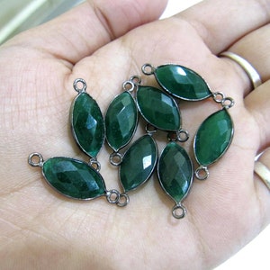 Puede incluir: Un grupo de diez conectores de piedra preciosa verde con bucles de metal plateados. Los conectores son de forma ovalada y tienen un acabado facetado.