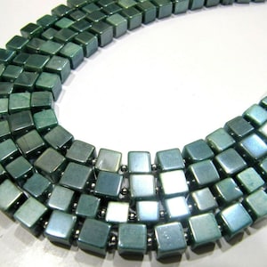 Puede incluir: Un collar hecho de varias hileras de cuentas cuadradas. Las cuentas son de color verde azulado oscuro con un ligero brillo.