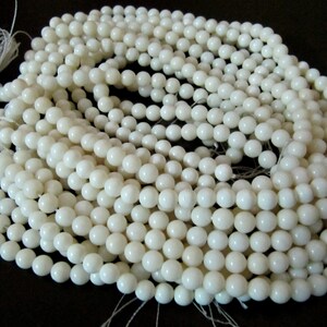 May include: A strand of white round shell beads. The beads are smooth and polished, and they are strung on a white thread.