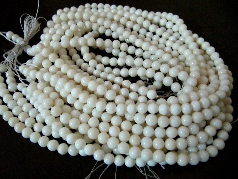 May include: A strand of white round shell beads. The beads are smooth and polished, and they are strung on a white thread.