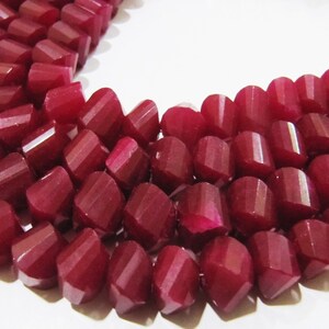 May include: A strand of deep red gemstone beads, each bead is faceted and has a slightly rounded shape. The beads are strung together on a clear thread.