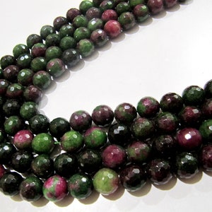 May include: A strand of faceted green and pink gemstone beads. The beads are round and have a faceted finish. The beads are strung on a clear thread.