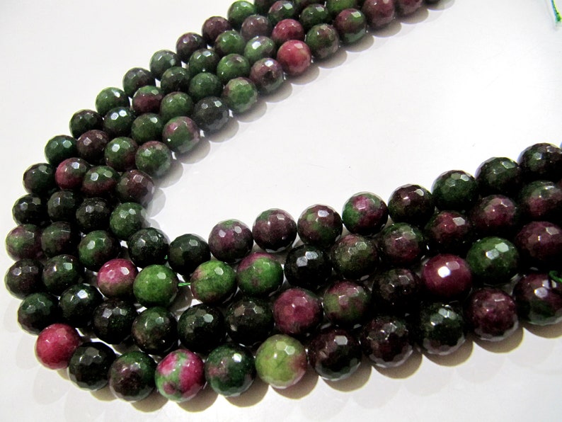May include: A strand of faceted green and pink gemstone beads. The beads are round and have a faceted finish. The beads are strung on a clear thread.