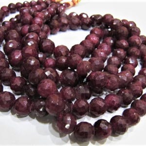 May include: A strand of deep red faceted gemstone beads. The beads are round and have a smooth, polished finish.