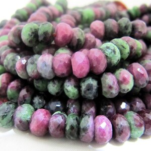 May include: Close-up of a strand of faceted beads. The beads are a mix of colors, including deep red, green, and gray. The beads are strung together, creating a textured and colorful pattern. The beads are likely made of natural stone.