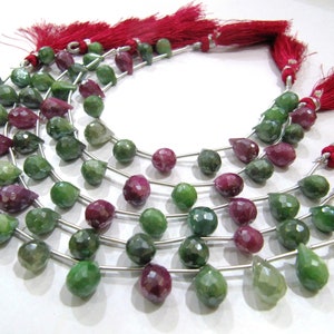 May include: A strand of faceted gemstone beads in shades of green and red. The beads are teardrop shaped and strung on silver wire. The strand is finished with red tassels.